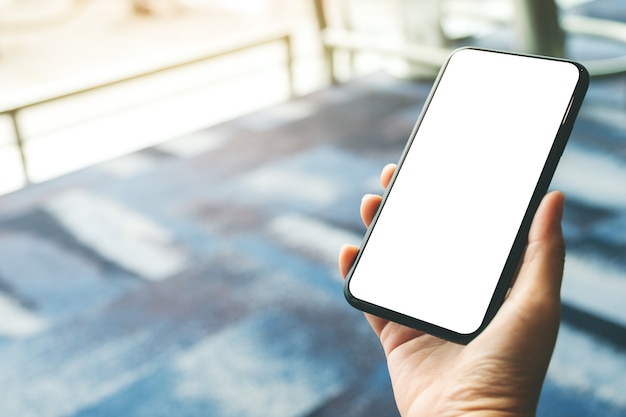 Immagine mockup delle mani di una donna che tiene e usa un telefono cellulare nero con schermo vuoto mentre è seduta in aeroporto