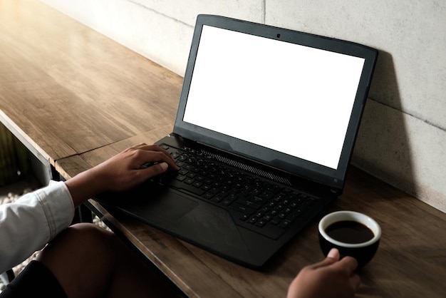 Immagine mockup di un uomo che utilizza e lavora su un computer portatile con uno schermo bianco vuoto con una tazza di caffè su un tavolo di legno