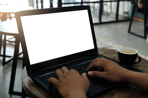 Immagine mockup di un uomo che utilizza e lavora su un computer portatile con uno schermo bianco vuoto con una tazza di caffè sul tavolo di legno nella caffetteria