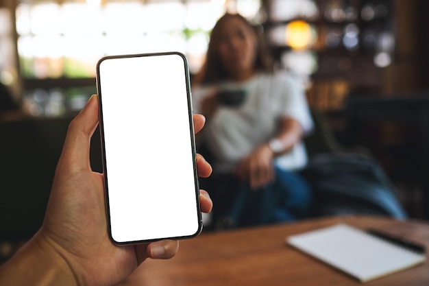 Immagine mockup di un uomo in possesso di un telefono cellulare con schermo bianco vuoto con una donna sullo sfondo