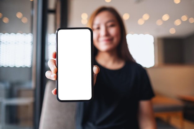 Immagine mockup di una bella donna asiatica che tiene e mostra un telefono cellulare con schermo bianco vuoto