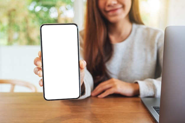 Immagine mockup di una bella donna che tiene e mostra un telefono cellulare con schermo bianco vuoto