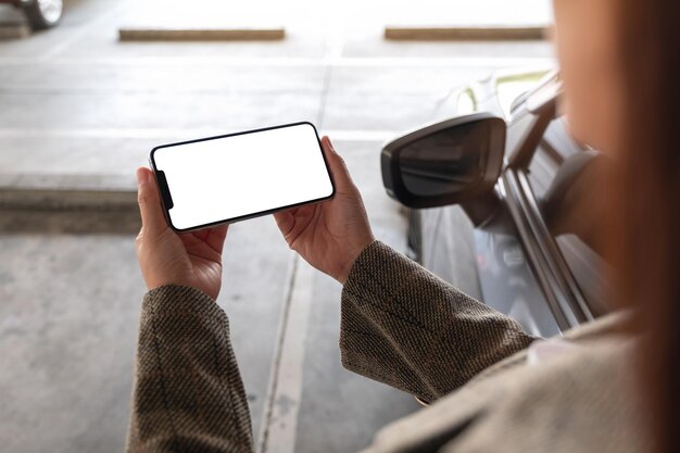 Immagine mockup di una donna che tiene e usa il telefono cellulare con schermo bianco vuoto accanto all'auto nel parcheggio