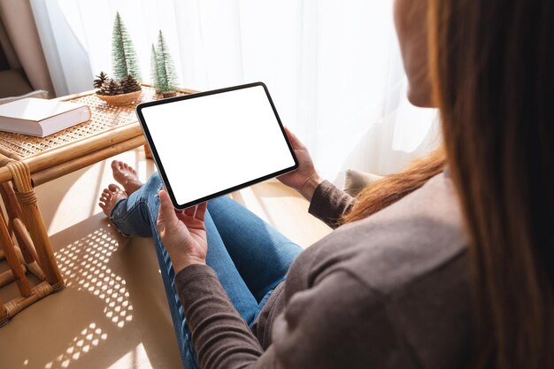 Immagine mockup di una donna che tiene e utilizza tablet pc con schermo bianco desktop vuoto a casa