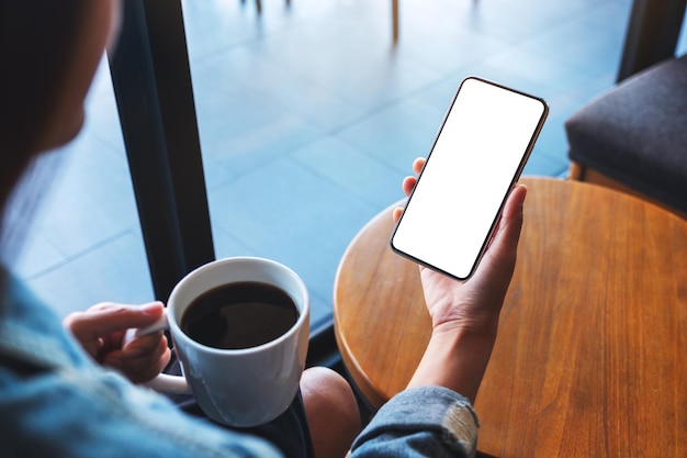 Immagine mockup di una donna che tiene il telefono cellulare con lo schermo del desktop bianco vuoto mentre beve il caffè