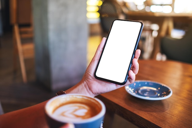 Immagine mockup di una donna che tiene il telefono cellulare con lo schermo del desktop bianco vuoto mentre beve il caffè