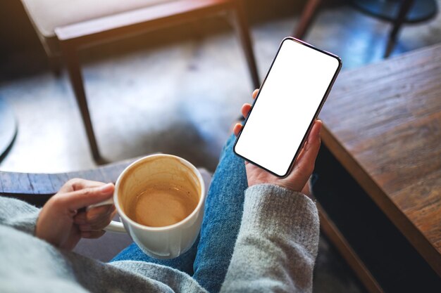 Immagine mockup di una donna che tiene il telefono cellulare con lo schermo del desktop bianco vuoto mentre beve il caffè