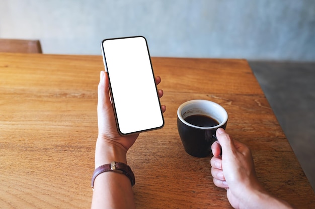 Immagine mockup di una donna che tiene il telefono cellulare con lo schermo del desktop bianco vuoto mentre beve il caffè