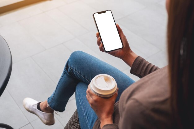 Immagine mockup di una donna che tiene il telefono cellulare con lo schermo del desktop bianco vuoto mentre beve il caffè