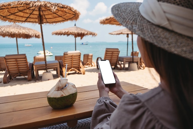 Immagine mockup di una donna che tiene il telefono cellulare con lo schermo del desktop vuoto mentre è seduto sulla spiaggia