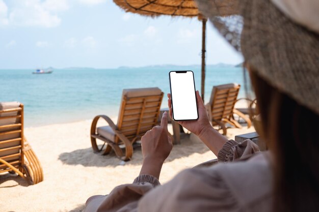 Immagine mockup di una donna che tiene il telefono cellulare con lo schermo del desktop vuoto mentre è seduto sulla spiaggia