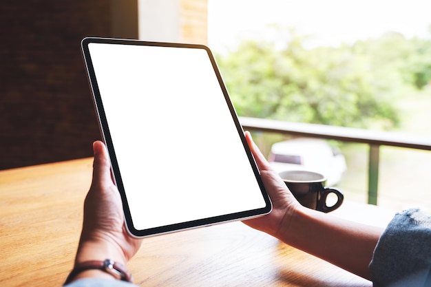 Immagine mockup di una donna che tiene in mano un tablet digitale con uno schermo desktop bianco vuoto in un caffè