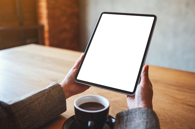 Immagine mockup di una donna che tiene in mano un tablet pc nero con schermo bianco vuoto con una tazza di caffè sul tavolo