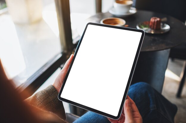 Immagine mockup di una donna che tiene in mano un tablet pc nero con schermo bianco vuoto in un caffè