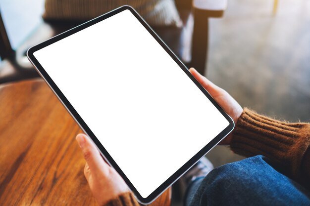 Immagine mockup di una donna che tiene in mano un tablet pc nero con schermo bianco vuoto su un tavolo di legno