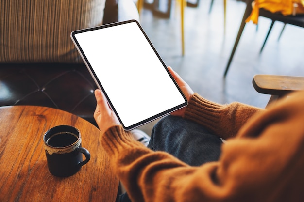 Immagine mockup di una donna che tiene in mano un tablet pc nero con schermo bianco vuoto su un tavolo di legno