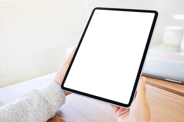 Immagine mockup di una donna che tiene in mano un tablet pc nero con schermo bianco vuoto su un tavolo di legno