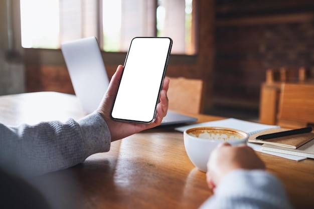 Immagine mockup di una donna che tiene in mano un telefono cellulare con uno schermo desktop bianco vuoto mentre beve caffè