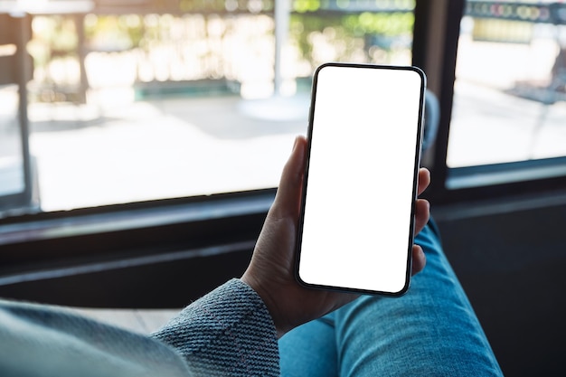 Immagine mockup di una donna che tiene in mano un telefono cellulare con uno schermo desktop bianco vuoto mentre è seduta al bar