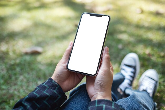 Immagine mockup di una donna che tiene in mano un telefono cellulare nero con schermo bianco vuoto mentre è seduta all'aperto