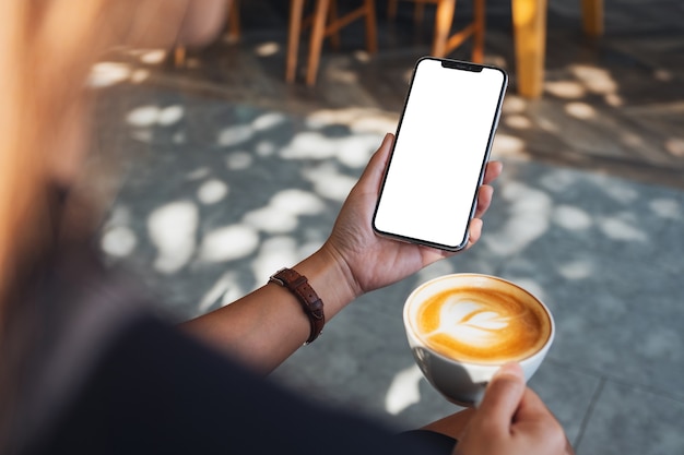 Immagine mockup di una donna che tiene in mano un telefono cellulare nero con schermo vuoto mentre beve caffè