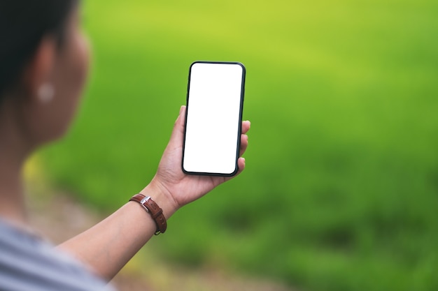 Immagine mockup di una donna che tiene in mano un telefono cellulare nero con uno schermo desktop vuoto con sfocatura dello sfondo verde della natura