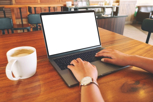 Immagine mockup di una donna che usa e digita sul computer portatile con schermo bianco vuoto e tazza di caffè su un tavolo di legno