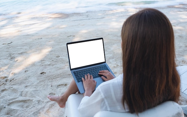 Immagine mockup di una donna che usa e digita sul computer portatile con schermo desktop vuoto mentre è seduto sulla spiaggia