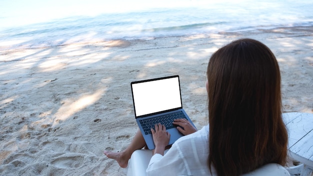 Immagine mockup di una donna che usa e digita sul computer portatile con schermo desktop vuoto mentre è seduto sulla spiaggia