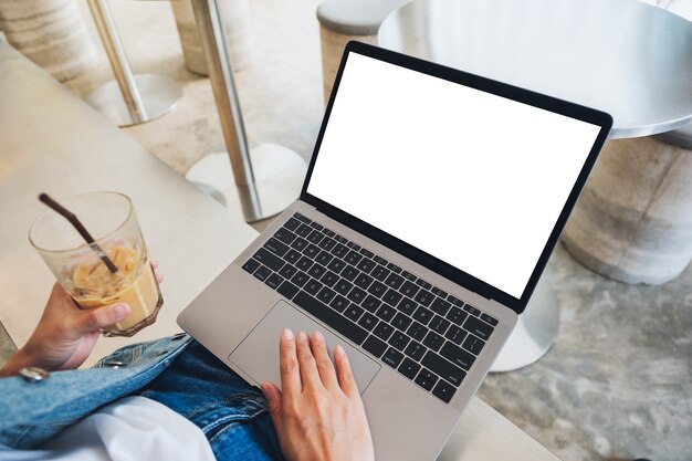 Immagine mockup di una donna che usa e tocca il touchpad del computer portatile con uno schermo desktop bianco vuoto mentre beve caffè