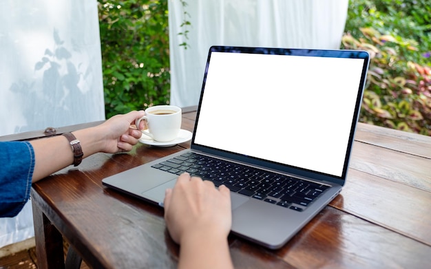 Immagine mockup di una donna che usa e tocca il touchpad del laptop con lo schermo del desktop bianco vuoto mentre beve caffè all'aperto