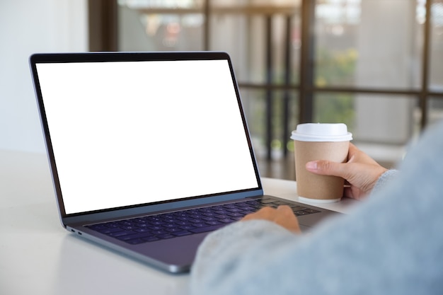 Immagine mockup di una donna che usa e tocca il touchpad del laptop con uno schermo desktop bianco vuoto mentre beve caffè