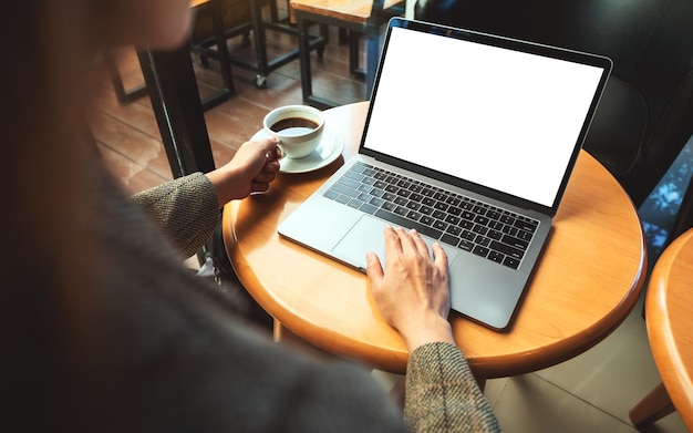 Immagine mockup di una donna che usa e tocca il touchpad del laptop con uno schermo desktop bianco vuoto mentre beve caffè