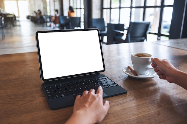 Immagine mockup di una donna che usa e tocca il touchpad della tavoletta digitale con schermo desktop bianco vuoto mentre beve caffè nella caffetteria