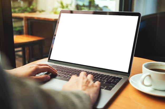 Immagine mockup di una donna che utilizza e digita sul computer portatile con schermo desktop bianco vuoto in un caffè