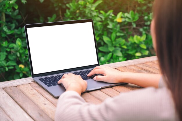 Immagine mockup di una donna che utilizza e digita sul computer portatile con schermo desktop bianco vuoto su un tavolo di legno