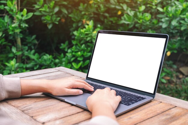 Immagine mockup di una donna che utilizza e digita sul computer portatile con schermo desktop bianco vuoto su un tavolo di legno