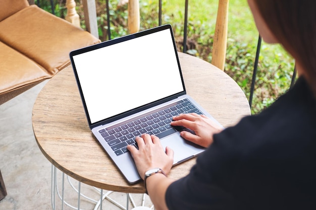 Immagine mockup di una donna che utilizza e digita sulla tastiera del computer portatile con schermo desktop bianco vuoto sul tavolo di legno