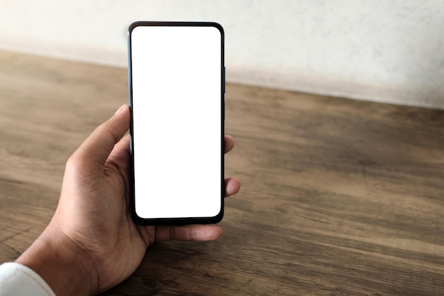 Immagine mockup di una mano che tiene il telefono cellulare con schermo vuoto sul tavolo di legno