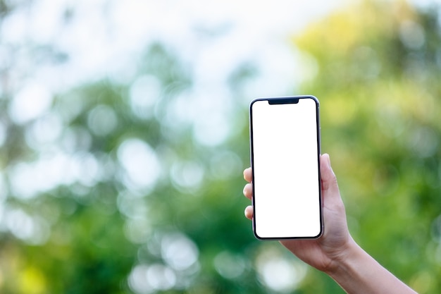 Immagine mockup di una mano che tiene un telefono cellulare nero con schermo desktop vuoto con sfondo verde natura