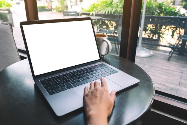 Immagine mockup di una mano che usa e tocca il touchpad del laptop con uno schermo desktop bianco vuoto con una tazza di caffè sul tavolo