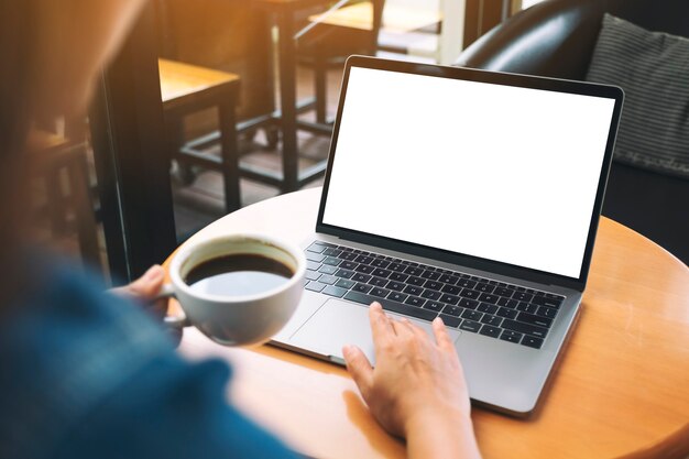 Immagine mockup di una mano che usa e tocca il touchpad del laptop con uno schermo desktop bianco vuoto mentre beve caffè