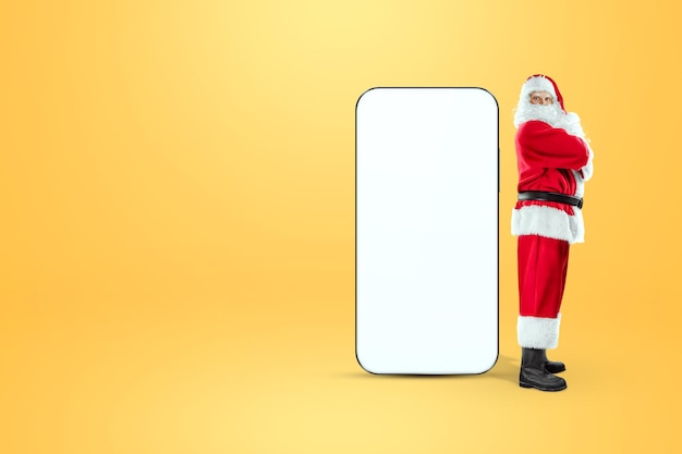 Immagine mockup per smartphone, ambiente per mostrare il design di app mobili, sfondo creativo. Smartphone per la tua pubblicità. Babbo Natale è in piedi accanto a un grande smartphone. Pubblicità di Natale.