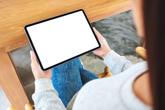 Immagine mockup vista dall'alto di una donna che tiene in mano un tablet pc nero con uno schermo desktop bianco vuoto