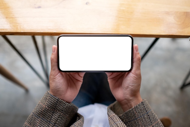 Immagine mockup vista dall'alto di una donna che tiene in mano un telefono cellulare con schermo bianco vuoto mentre è seduta in ufficio