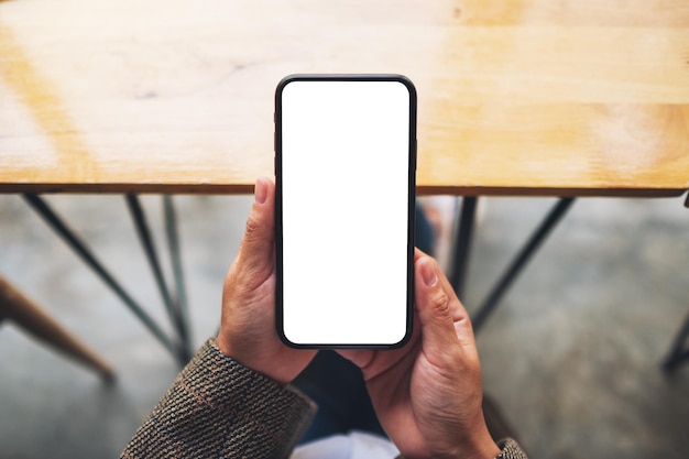 Immagine mockup vista dall'alto di una donna che tiene in mano un telefono cellulare con schermo bianco vuoto mentre è seduta in ufficio