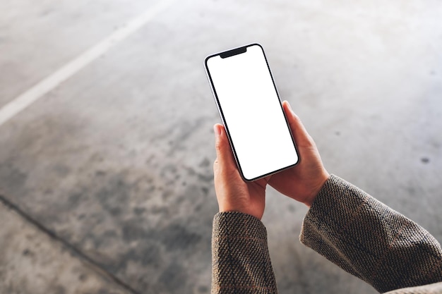 Immagine mockup vista dall'alto di una donna che tiene in mano un telefono cellulare con schermo bianco vuoto per strada