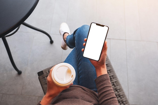 Immagine mockup vista dall'alto di una donna che tiene in mano un telefono cellulare con uno schermo desktop bianco vuoto mentre beve caffè