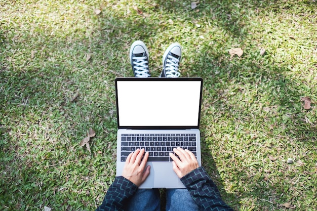 Immagine mockup vista dall'alto di una donna che usa e digita sul laptop con schermo bianco vuoto mentre è seduta all'aperto