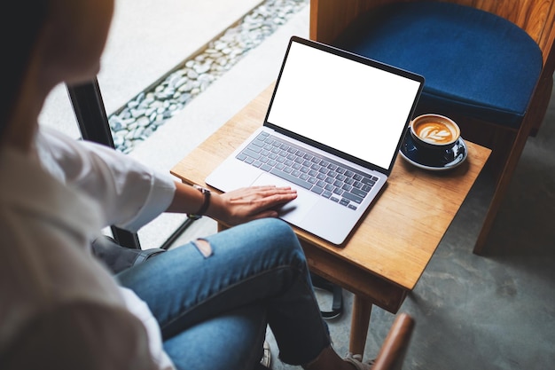 Immagine mockup vista dall'alto di una donna che usa e tocca il touchpad del laptop con uno schermo desktop bianco vuoto su un tavolo di legno